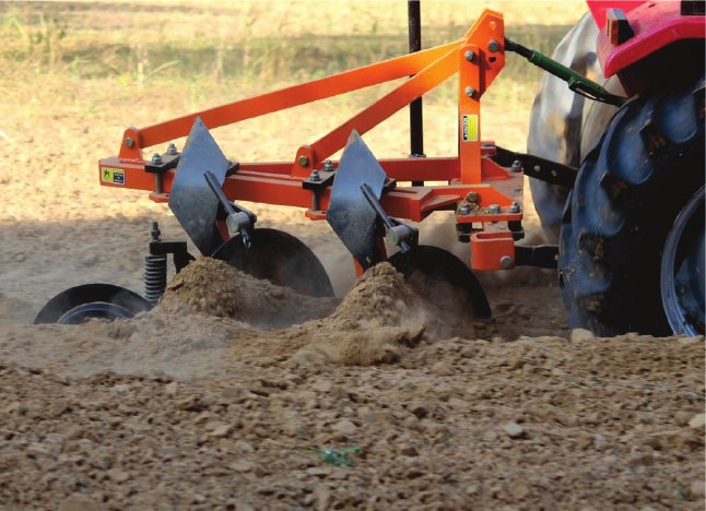 Reversible plough working a field behind a tractor